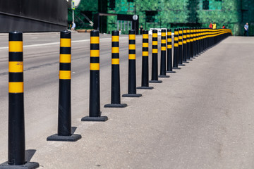 Closeup parking limiter black round bars with a yellow stripes between the roadway and the sidewalk. Concept traffic restriction, no access to drive, cityscape, repeating print