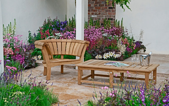 A contemporary garden with terraced area and stylish wooden furniture surrounded by colourful flowering borders