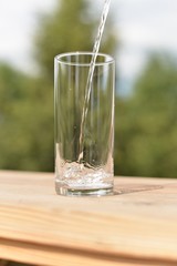 A stream of water flowing into an empty transparent glass standing on a wooden board.