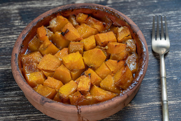 Baked yellow pumpkin with honey, olive oil and spices on a plate on the wooden table. Vegetarian food. Closeup