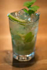 Refreshing mint cocktail mojito with rum and lime, cold drink or beverage with ice on white wooden background, top view