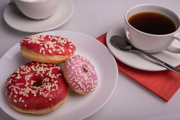 Obraz na płótnie Canvas Three donuts coated with pink icing with sprinkles and cup of coffee on the table.