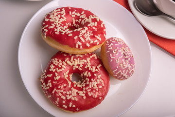 Three donuts coated with pink icing with sprinkles on the table.