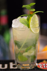 Refreshing mint cocktail mojito with rum and lime, cold drink or beverage with ice on white wooden background, top view