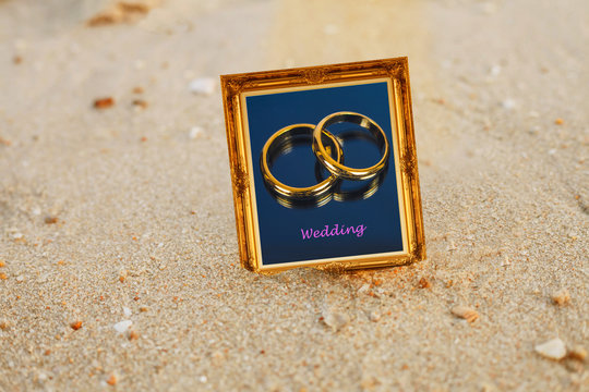 Golden wedding ring in vintage gold picture frame on sand beach.