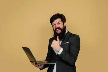 Excited man with laptop computer shows thumbs up. Businessman working with notebook in office. Business man with computer at workplace. Technology, networking and internet.