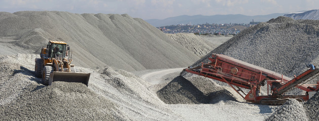 Wheel loader excavator and mobile crusher against the background of crushed stone hills, panorama....