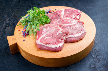 Traditionelle rohe deutsche Ochsenbacken angeboten als closeup mit Kräutern und Gewürzen auf einem Modern Design Holz Schneidebrett