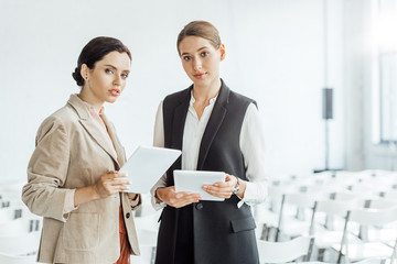 two attractive colleagues in formal wear holding digital tablets in conference hall