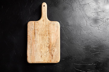 A Cutting board with handle on black stone table. Empty pine wooden chopping board on dark...