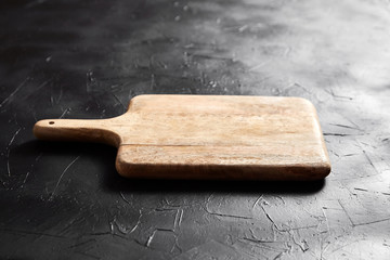Fototapeta premium A Cutting board with handle on black stone table. Empty pine wooden chopping board on dark background, side view