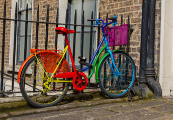 Colorful multi-colored bike bicycle in bright rainbow colors. At railings outside brick wall building. Red, orange, yellow, green, blue, indigo and violet. Dublin Ireland