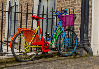Colorful multi-colored bike bicycle in bright rainbow colors. At railings outside brick wall...
