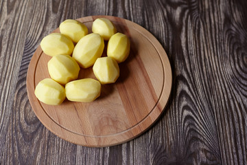 Fototapeta na wymiar Potatoes on wooden chopping board on brown table. Cooking food from natural products. Root vegetable. Raw ingredient: uncooked whole peeled potatoes