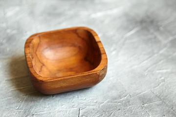 One empty wooden bowl on grey background. Single square salad bowl on stone table with black paint stains, side view