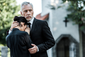 sad senior man hugging upset woman near church