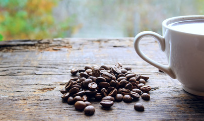 A coffee cup with hot coffee is on the table. Near coffee beans. Blurred background. Concept - Morning Breakfast