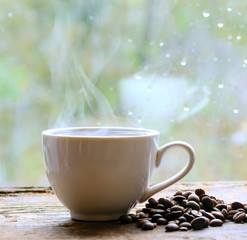 A coffee cup with hot coffee is on the table. Near coffee beans. Blurred background. Concept - Morning Breakfast