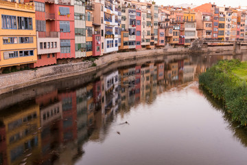 Colorful yellow and orange houses reflected in water river Onyar, in Girona, Catalonia, Spain.