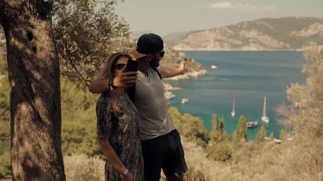 Lovers Taking Self Photo And Answer To Video Call On Sea Mountains.Selfie Couple On Beautiful Place.Couple Taking Selfie On Seashore Mediterranean Coast.Pair Takes Pictures On Smartphone On Seashore.