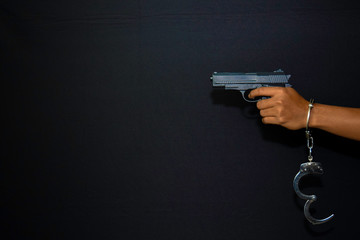 asian man holds gun and handcuffs hanging on a hand isolated on black background