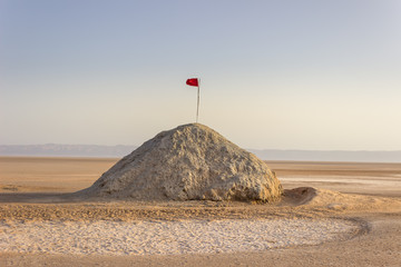 Chott el Djerid, the largest salt lake flats in Sahara desert in Tunisia and Tunisian red flag at the top of the hill under the blue sky