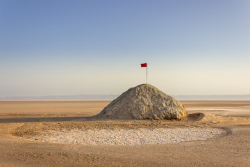 Chott el Djerid, the largest salt lake flats in Sahara desert in Tunisia and Tunisian red flag at the top of the hill under the blue sky
