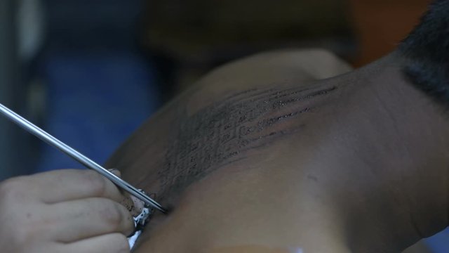 Tattooing concepts. The artist is tattooing a Thai style pattern on the skin with a pointed metal. 4k Resolution.