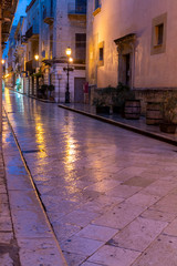 Fototapeta na wymiar Old street in Marsala at night in rain with reflection of street lights on water, Sicily, Italy