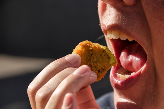 Human hand bringing a traditional Dutch bitterbal (meatball) dipped in mustard to a wide open mouth