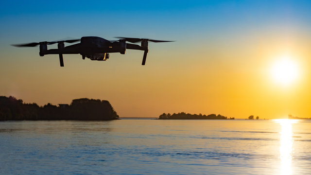Drone flight at sunset. The quadcopter flies over the water against the backdrop of the setting sun. Panorama of the lake at sunset. The drone takes beautiful pictures. Hobby - manage quadcopter.