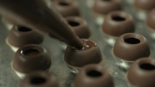 Close up of piping bag filling chocolate into tray of round chocolate mold
