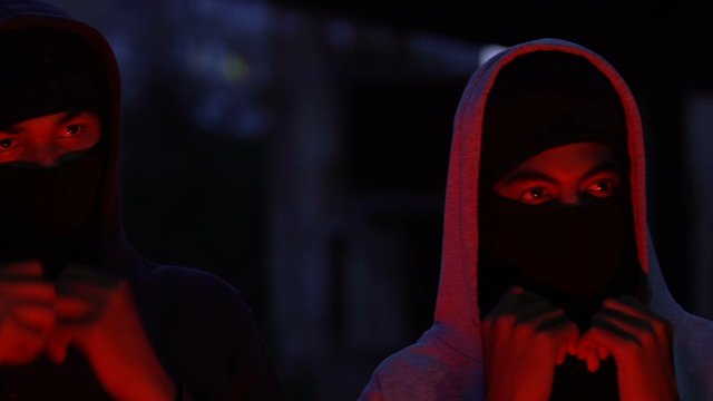 Male hooligans wearing balaclava at night, preparing for crime, red lights