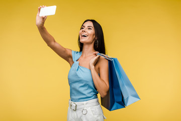 happy woman holding shopping bags and taking selfie on smartphone on orange