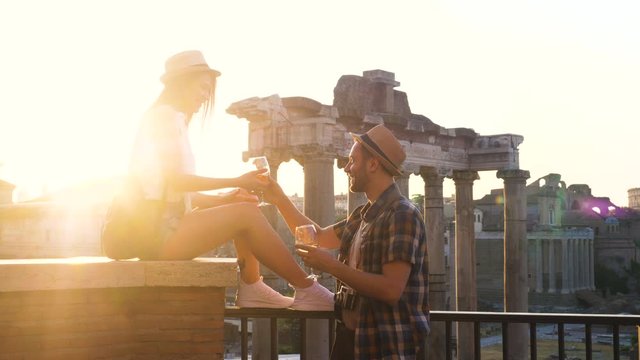 Young couple tourist with bottle of white wine and glasses at Roman Forum at sunrise. Historical imperial Foro Romano in Rome, Italy from panoramic point of view.