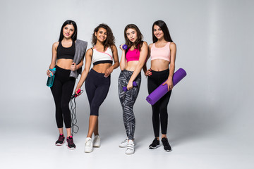 Fototapeta premium Four fitness girls in sportwear holding exercises equipment isolated on white background