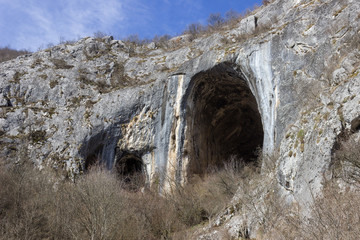 Huge, impressive entrance in to the cave Vladikine ploce on Old mountain, Serbia, blue sky and foreground bushes