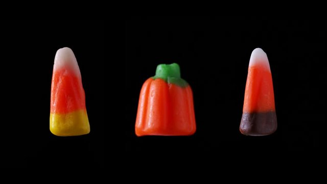 An assortment of candy corn Halloween candy is seen floating and rotating with a black back drop.