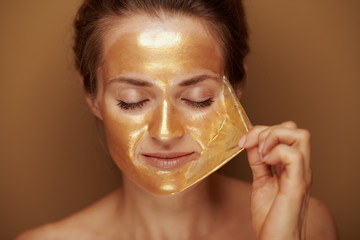 modern woman removing golden mask against beige background