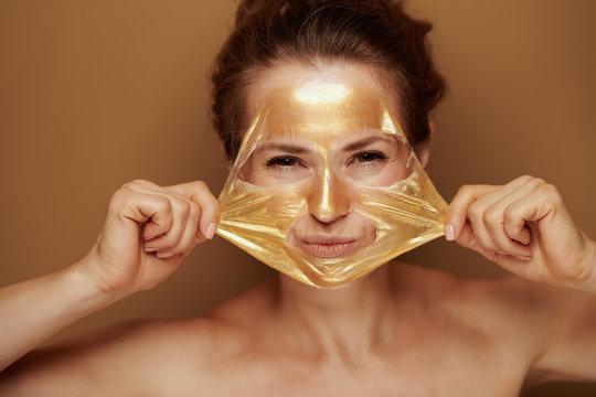 woman removing golden mask isolated on brown background