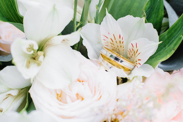 Wedding engagement rings of yellow and white gold are on the wedding bouquet, white flowers