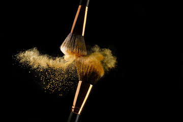 Cosmetic brush with golden powder spreading on black background