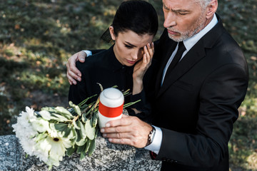 overhead view of senior man hugging upset woman while holding mortuary urn