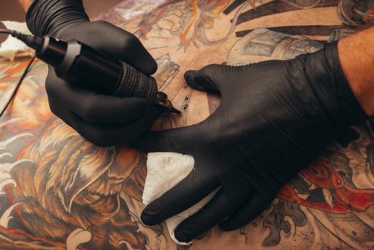 Close up tattoo machine. Tattooing. Man creating picture on his back by a professional tattoo artist.