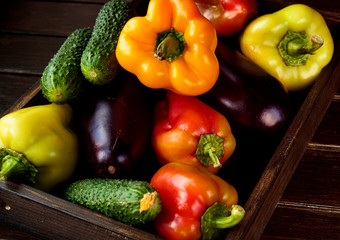 Autumn vegetables (peppers, eggplant, cucumbers) in a wooden box on a wooden table. The concept of healthy and diet food.