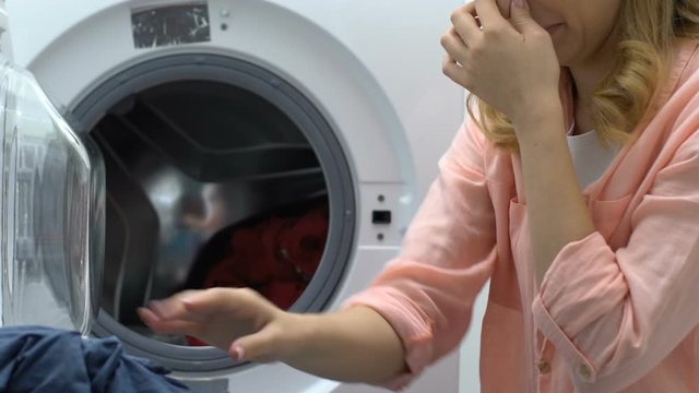 Lady taking out denim jacket out of washing machine and smelling it, disgust
