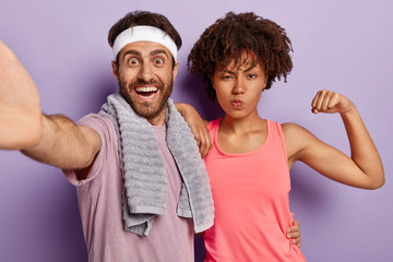 Happy diverse woman and man take selfie, dressed in casual clothes, stand closely to each other, go in for sport, stand against purple background. People, wellness, fitness and workout concept