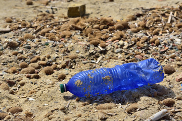 A blue old crushed plastic bottle lies as trash on the beach in the sun.