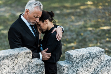 selective focus of senior man hugging woman near tombs