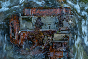 Old rusty engine lying among stones in the water.